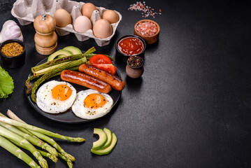 A delicious nourishing breakfast with fried eggs, sausages, asparagus, tomatoes, avocado, spices and herbs