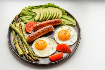 A delicious nourishing breakfast with fried eggs, sausages, asparagus, tomatoes, avocado, spices and herbs