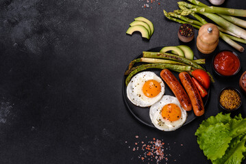 A delicious nourishing breakfast with fried eggs, sausages, asparagus, tomatoes, avocado, spices and herbs