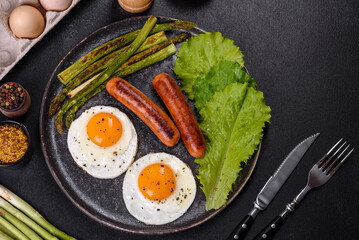 A delicious nourishing breakfast with fried eggs, sausages, asparagus, tomatoes, avocado, spices and herbs