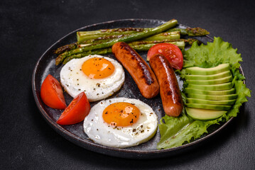 A delicious nourishing breakfast with fried eggs, sausages, asparagus, tomatoes, avocado, spices and herbs