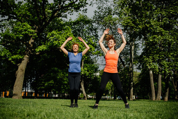 Two women perform aerobic exercises in a city park