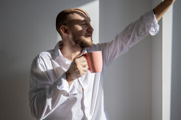 Young man closing his eyes holding a cup of coffee under the sun.