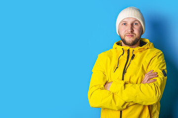 Young man in a yellow jacket with crossed arms on a blue background