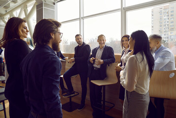 Team of business people communicating with each other. Group of happy positive young men and women standing in modern office, talking, sharing impressions after corporate meeting or training session