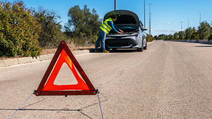 Young man preparing a red triangle to warn other road users of car breakdown