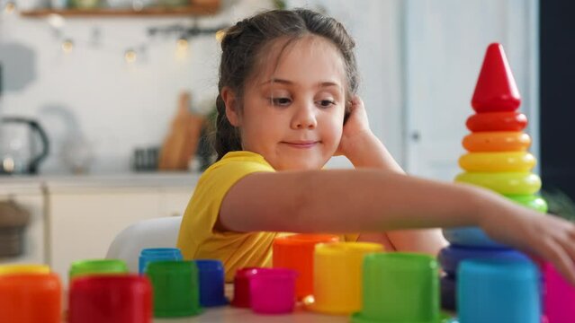 Happy girl at table.Child plays with colored toys at table. Girl in room at home. Child building house. Girl with colorful toys at table. Children's room preschool education.Little kid playing at home