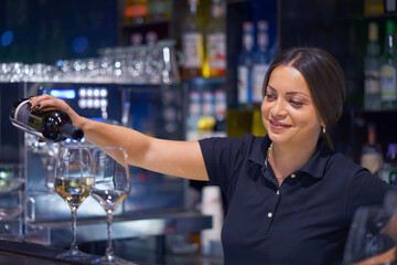 Bartender girl in hotel pours white wine into a glass from a bottle