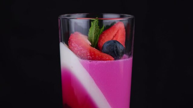 Fruit jelly with strawberries and blueberries in a rotating glass on a black background, a beautiful rotating dessert