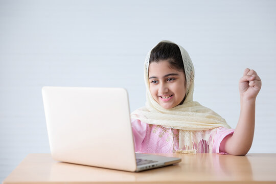 Muslim Girl Using A Laptop Computer And Raised Hand For Celebrating Good News On The Table