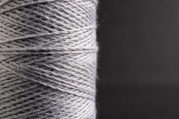 detalle de un carrete de hilo de algodón color gris sobre fondo obscuro