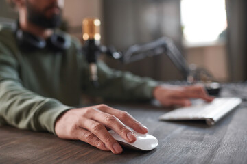 Horizontal selective focus shot of unrecognizable blogger at desk in loft room typing something on computer or playing game