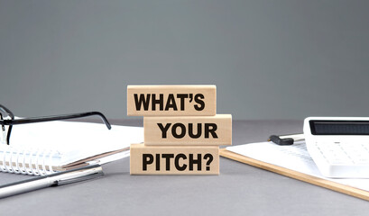 What's Your Pitch text on wooden block with notebook,chart and calculator, grey background