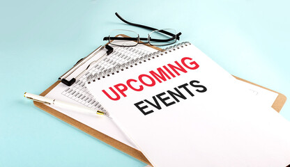 UPCOMING EVENTS text on notepad on clipboard with chart on blue background, concept closeup. Business and finance concept