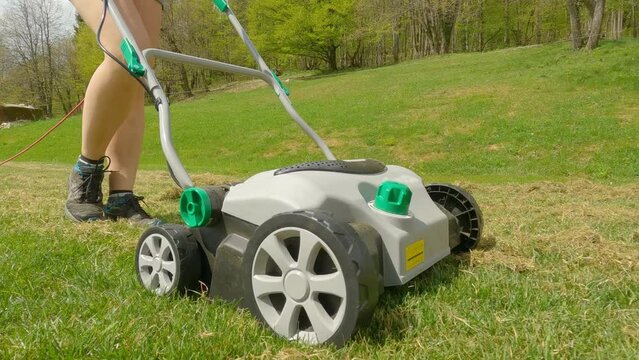 SLOW MOTION: Young woman using lawn aerator to grow healthier and thicker lawn. Spring backyard garden work for lawn growth enhancement. Practical gardening machinery for efficiency at landscaping.