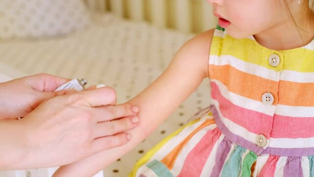 Woman applies a cream from a tube to unhealthy, disease skin of child suffering from atopic dermatitis. Red rough spots on the crook of baby's arms. Ointment for relieving symptoms of allergic disease