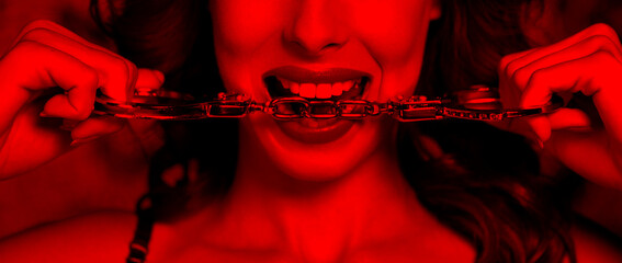 Sexy woman in red light bite handcuffs - obrazy, fototapety, plakaty