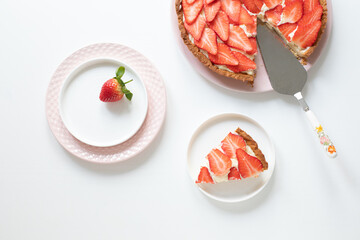 Delicious tart with custard cream and strawberries on a white table. Plates and spatula for dough application. Piece of grated on a plate. View from above. - 506137913
