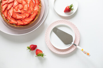 Delicious tart with custard cream and strawberries on a white table. Plates and spatula for dough application. View from above. - 506137917