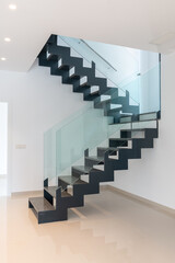 A modern staircase. Openwork stairs made of metal and marble, and glass balustrades. - 506137943