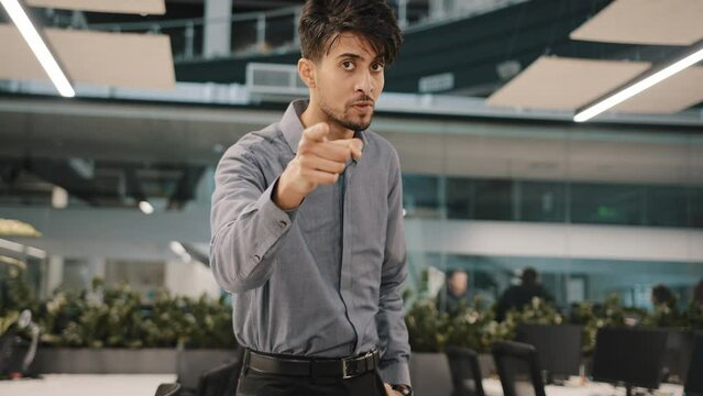 Smiling indian arabian confident male business man adult guy director stand in confident pose point index finger at camera hey you gesture make choice tell corporate information gesticulation indoor