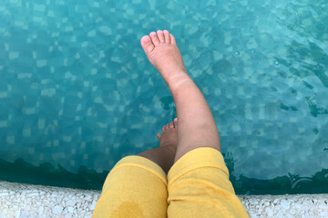 Naughty children's swarthy legs in yellow shorts splash water in the pool