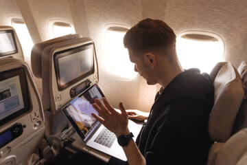 A man sitting into an airplane. Male passenger traveling aircraft cabin. Business work from plane on laptop. Wireless internet working on plain while traveling.