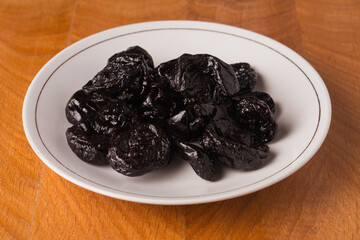 Prune dried fruit lies in a bunch in a white plate on a wooden board