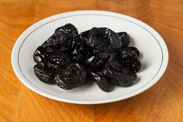 Prune dried fruit lies in a bunch in a white plate on a wooden board