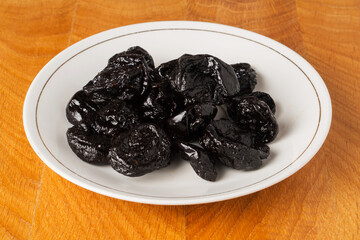 Prune dried fruit lies in a bunch in a white plate on a wooden board