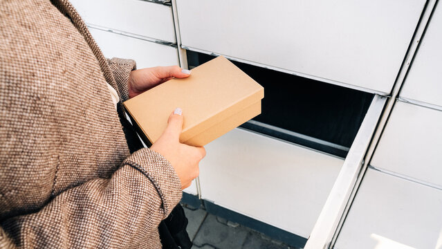 Pickup parcel. Courier box in woman hands at post delivery automat terminal. Self service post terminal and parcel delivery concept.