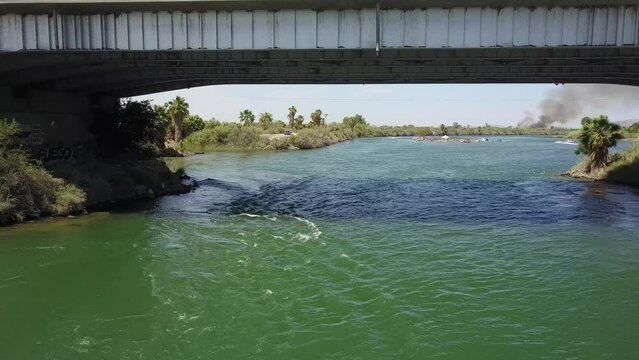 aerial footage of the green flowing waters of the Colorado river with metal bridge over the water and people in boats and riding jet skis with blue sky at Quechan Park in Blythe California USA