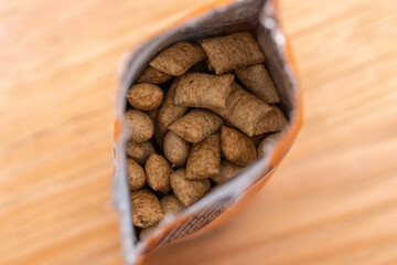Open package of dry dog and cat treats viewed from above on a wooden table. Pet food.