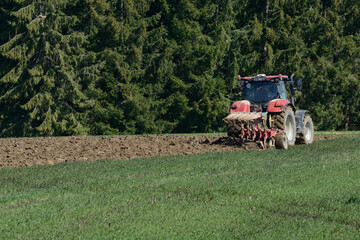 Red tractor against a green background ploughing a corn field