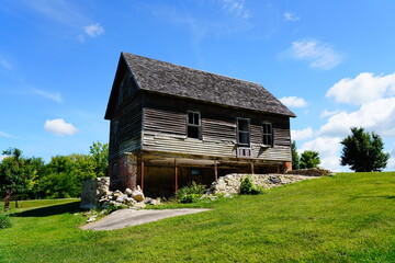 An old abandoned vintage wooden home sits on a hillside in Ripon, Wisconsin during beautiful cloudy July weather.