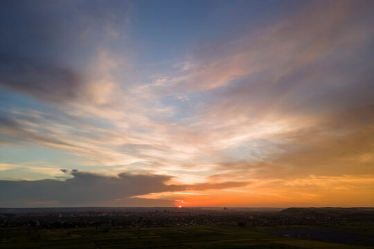 Bright colorful sunset sky with setting sun and vibrant clouds over dark landscape © bilanol