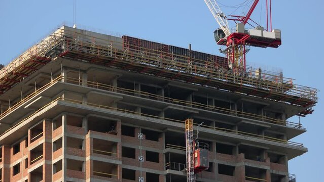 Building constriction site with scaffolding and crane. Red crane machine in action. Blue sky background.