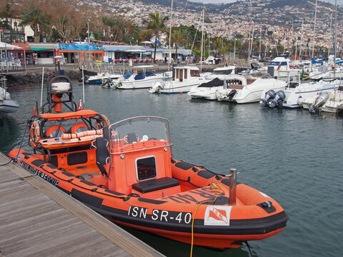 unchal, madeira, portugal - 14 march 2019: an orange rescue boat belonging to the Portuguese lsn national lifeboat service moored in the marina with yachts and waterside cafes in the background