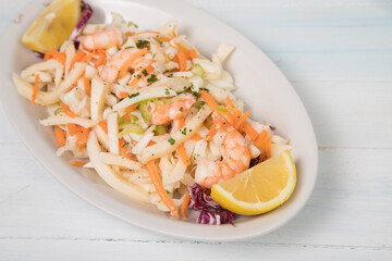 Seafood appetizer, seafood salad with prawns, squid in a large white serving dish. Typical Italian antipasto on wooden background