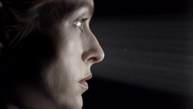 Side profile of a female face staring into a light shaft in a studio with black background