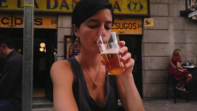 Beautiful Caucasian woman drinks beer in a bar in Madrid (Spain). Spanish girl sitting on a terrace enjoying a beer. 4K summer. Woman enjoying a beer in Spain.