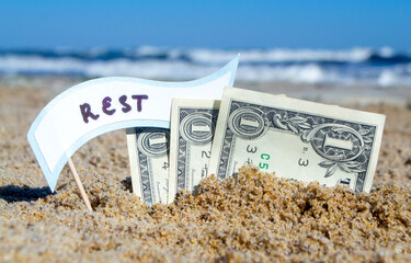 Paper bills one dollars, small stick with paper speech bubble with word Rest buried in sand beach...