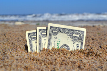 Paper bills one dollar buried in the sand on the beach against backdrop of sea close-up. American...