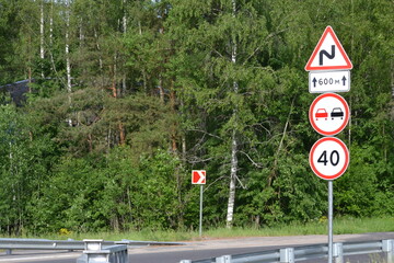 Road signs on the road - speed limit, no overtaking, winding road - against the backdrop of a green forest