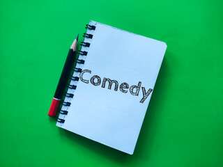 Pencil and notebook with Comedy writing on a green background.