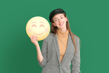 Happy young woman holding smiling emoticon on green background