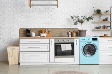 Interior of light modern kitchen with turquoise washing machine and white brick wall