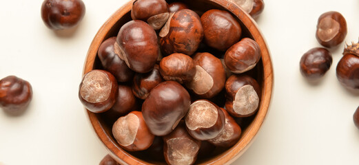 Bowl full of brown chestnuts on white background, top view