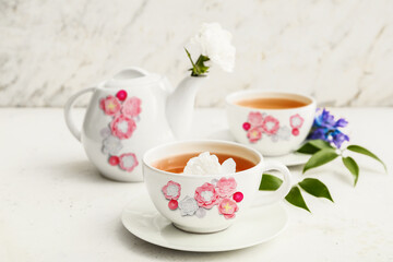Stylish tea pot and cups of hot beverage with flowers on light background