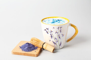 Stylish cup of tasty blue matcha latte with chasen and powder on light background